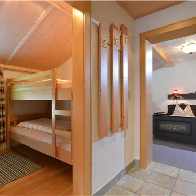 Ein gemütliches Schlafzimmer mit einem Etagenbett und einem klassischen Doppelbett. Der Raum hat Holzverkleidungen und eine warme Atmosphäre.