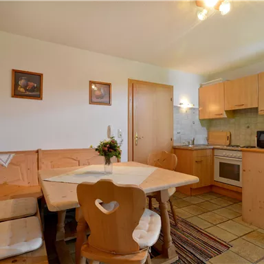 Eine gemütliche Küche mit einem Essbereich aus Holz und beige gefliesten Böden. Es gibt moderne Küchengeräte und dekorative Wandbilder.