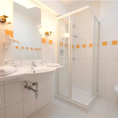 Ein modernes Badezimmer mit einer Dusche und einem Waschbecken. Die Wände sind hell gefliest und mit orangefarbenen Akzenten dekoriert.