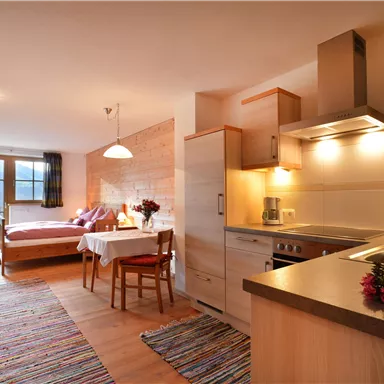 Eine moderne Wohnung mit einem Schlafzimmer und einer Küchenzeile. Der Raum ist hell und gemütlich, mit einem Tisch und Stühlen sowie einem schönen Teppich.