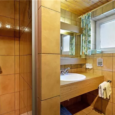 Ein modernes Badezimmer mit gefliesten Wänden und Holzdecke. Es gibt eine Dusche und ein Waschbecken mit Spiegel.