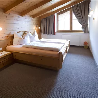 A cozy bedroom with wooden paneling. Two beds are placed side by side, and a window provides natural light.