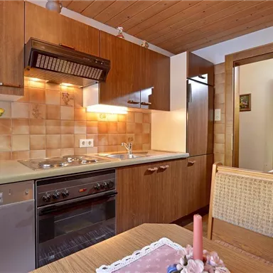 Eine kleine Küche mit Holzmöbeln und modernen Geräten. Der Raum ist gut beleuchtet und hat eine offene Tür zu einem weiteren Bereich.