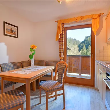 Ein gemütlicher Essbereich mit einem Tisch, Stühlen und einer Blumenvasen. Durch das Fenster hat man einen Blick auf die Berge und die Natur.