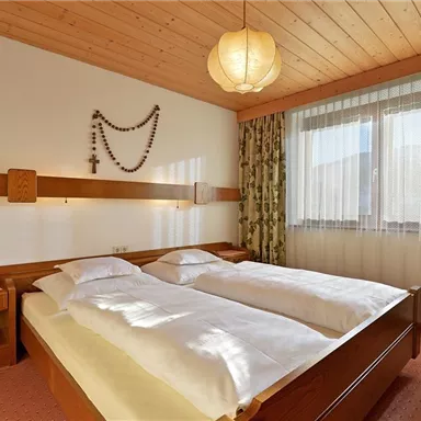 Ein gemütliches Schlafzimmer mit zwei Einzelbetten und einem Holzkopfteil. Die Fenster sind mit Vorhängen bedeckt, und die Wände sind mit Holzpaneelen gestaltet.