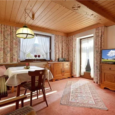 Ein gemütlicher Wohnraum mit Holzmöbeln und einem Tisch. Große Fenster lassen viel Licht herein und verleihen dem Raum eine einladende Atmosphäre.