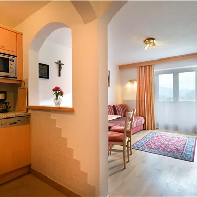 Eine moderne Kochküche mit Holzregalen und einem kleinen Essbereich. Der Raum hat große Fenster mit Vorhängen und einen hellen, einladenden Eindruck.