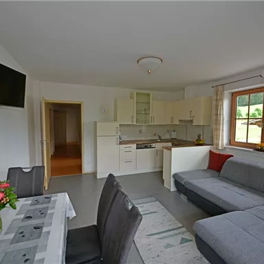 A modern kitchen with a cozy living room. The space is bright and inviting, with large windows and a beautiful dining table.