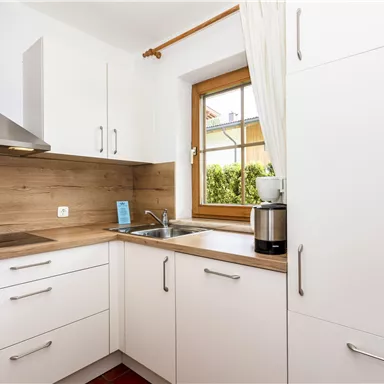 A modern kitchen with white cabinets and a wooden countertop. The window offers a view of the outdoors and provides plenty of natural light.