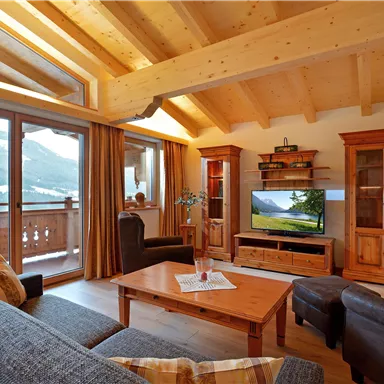 A cozy living room with a wooden ceiling and large windows. The room is modernly furnished and offers a view of the mountains.