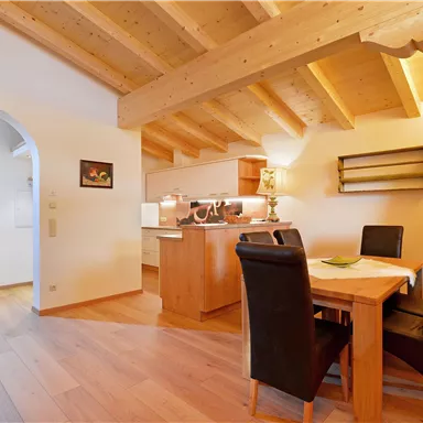 A cozy kitchen with a wooden beam ceiling and a dining table. The decor is modern and inviting.