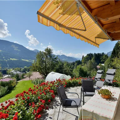 An inviting terrace with a view of the mountains and colorful flowers. The sun is shining and the surroundings are green and sunny.