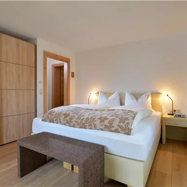 A modern bedroom with a comfortable double bed and wooden furniture. The warm colors create an inviting atmosphere.