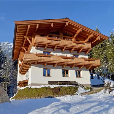 A beautiful chalet in the snow surrounded by trees. The blue sky creates a picturesque winter atmosphere.