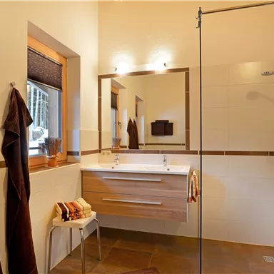 A modern bathroom with an open shower and wooden details. The walls are light and the lighting creates a pleasant atmosphere.