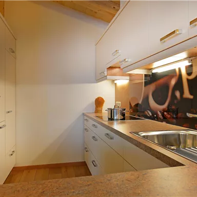 A modern kitchen with bright cabinets and a wooden countertop. In the background, coffee containers and a wall with an espresso motif are visible.
