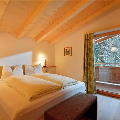 A cozy bedroom with a wooden ceiling and a large window. There are two beds and a view of nature.