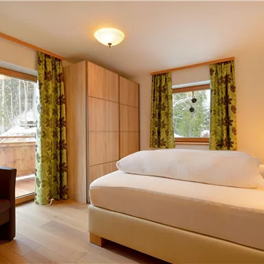 A cozy bedroom with a large bed and a beautiful view of nature. The green curtains create a vibrant atmosphere.