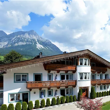 A picturesque building in alpine style with balconies and a beautiful view of the mountains. The surroundings are green and inviting.