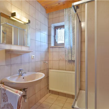 Ein modernes Badezimmer mit gefliesten Wänden und Holzdecken. Es verfügt über ein Waschbecken, eine Dusche und einen Heizkörper.
