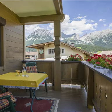 A cozy balcony with a yellow table and a view of majestic mountains. Colorful flowers beautify the surroundings and invite you to relax.