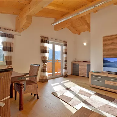 Ein modernes Wohnzimmer mit Holzdecken und großen Fenstern. Der Raum ist hell und gemütlich, mit einem Essbereich und einem Fernseher.