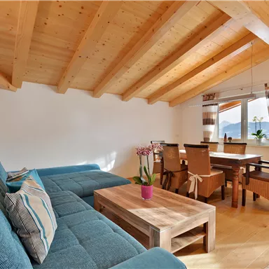 Ein helles Wohnzimmer mit Holzdecke und modernem Interieur. Eine bequeme Couch und ein Esstisch für gemütliche Zusammenkünfte sind vorhanden.