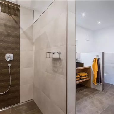 Ein modernes Badezimmer mit einer Dusche und hellen Fliesen. Handtücher liegen ordentlich auf einem Regal.