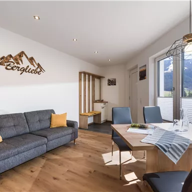 Ein modernes Wohnzimmer mit einem grauen Sofa, einem Esstisch und schönen Bergblick. Die Einrichtung ist hell und einladend, mit einem Holzdekor.