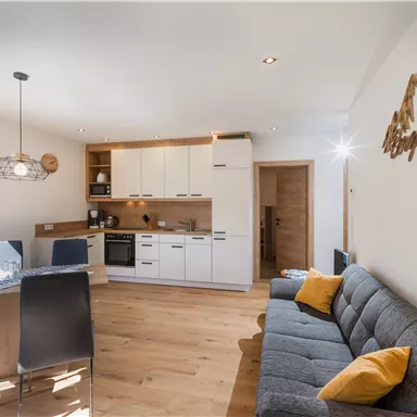 Eine moderne Küche mit einem gemütlichen Wohnbereich. Der Raum ist hell und freundlich mit Holzfußboden und einer einladenden Atmosphäre.