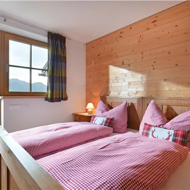 Ein gemütliches Schlafzimmer mit zwei Einzelbetten und Holzwänden. Große Fenster bieten einen schönen Blick auf die Berge.