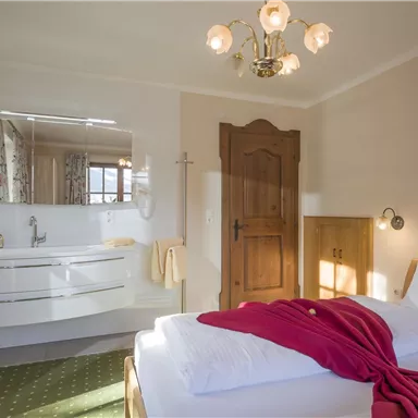 A cozy bedroom with a large bed and a modern bathroom. The walls are painted in bright colors, and a red plaid is laid on the bedspread.