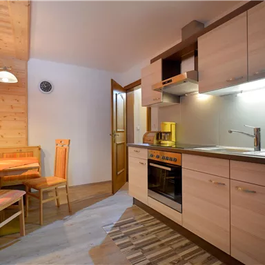 A modern kitchen with wooden cabinets and a dining area. The equipment includes a stove, a kettle, and a quiet atmosphere.