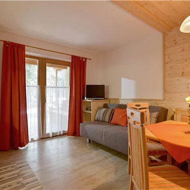 A cozy living space with a sofa, dining table, and a modern kitchenette. The red curtains and wooden paneling create a warm atmosphere.