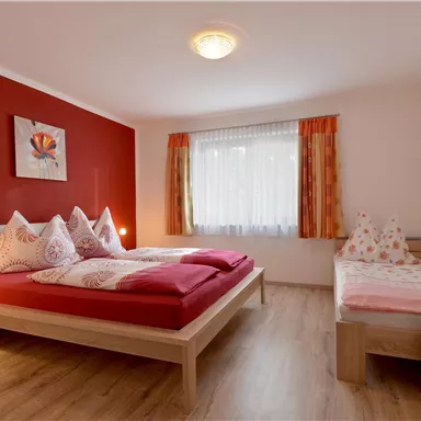 A cozy bedroom with red walls and a large bed. The room has large windows and a modern wardrobe.
