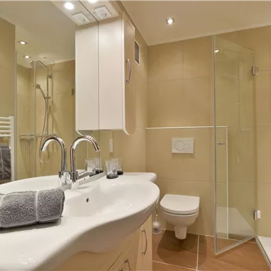A modern bathroom with a glass shower and a sink. The walls are in neutral colors and decorative towels are neatly arranged.