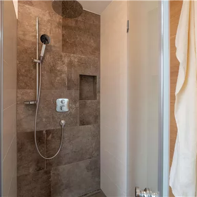 A modern shower with brown tiles and a clear shower wall. Towels hang on the wall, and the shower looks inviting.