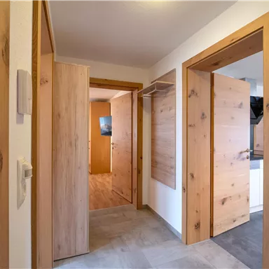 A bright hallway with wood doors and a modern design. The walls are plain and the floor tiles are in neutral colors.