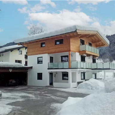 A modern house in the mountains, surrounded by snow. The sky is blue with a few clouds.
