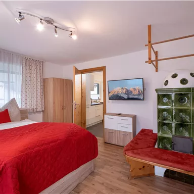 A cozy bedroom with a red bed and modern furniture. Partly country house style with a stove and a large window.