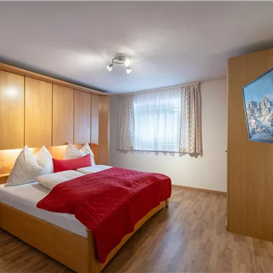 A cozy bedroom with a large bed and wooden cabinets. The room has a window with curtains and a television on the wall.