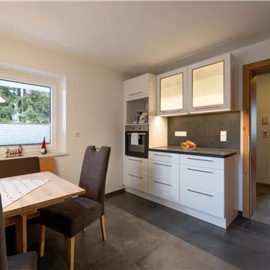 A modern kitchen with bright cabinets and a dining table. The room is well-lit and has large windows.