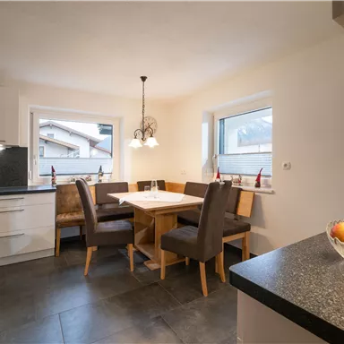 A modern kitchen with a dining area. The table is set for four people and there are large windows looking outside.