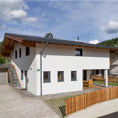 A modern two-story house with a wooden roof and white walls. The exterior features a terrace and a wooden fence.