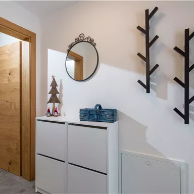 A bright entrance area with a wooden door. A mirror and decorative branches hang on the wall, next to which stands a storage cabinet.