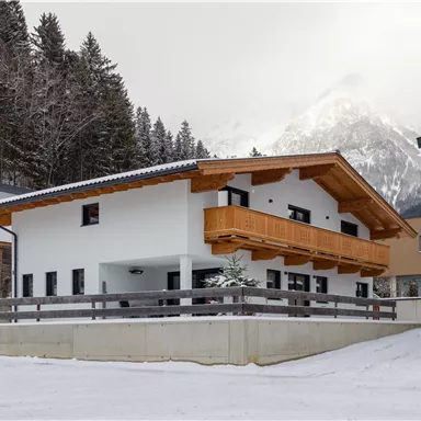 A modern house in a snow-covered landscape. In the background, mountains and trees can be seen.