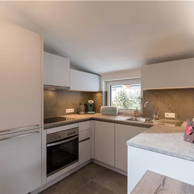 A modern kitchen with white cabinets and a gray countertop. The room has windows that let in light.