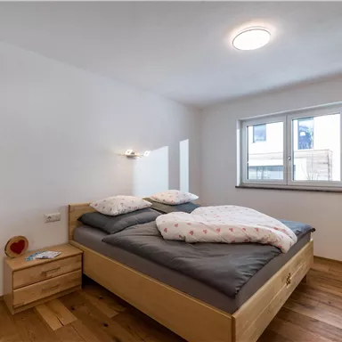 A cozy bedroom with a double bed and modern wooden furniture. The room has large windows that let in a lot of light.