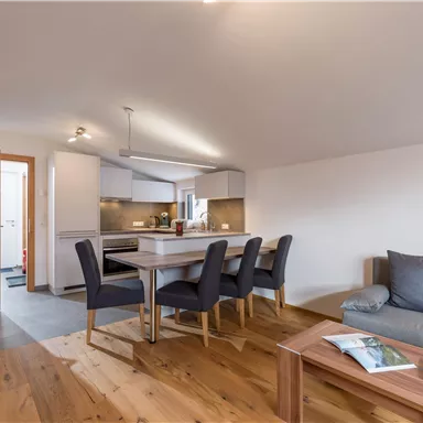 A modern apartment with an open living and dining area. There is a bright kitchenette and a cozy seating area.