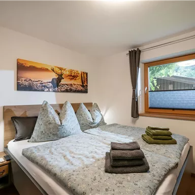 A cozy bedroom with a double bed and eye-catching pillows. Large windows provide plenty of daylight and a pleasant atmosphere.